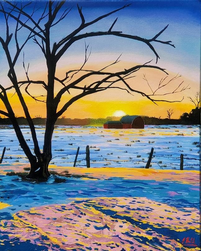 A lone bare tree and distant red barn at a vivid winter sunset, snow lit in blue, gold, and rose